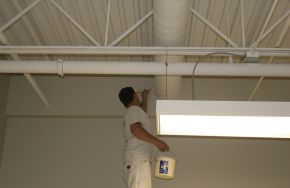 Man painting an industrial ceiling. What to Include in a Facility Maintenance Plan Template for Industrial or Commercial Use